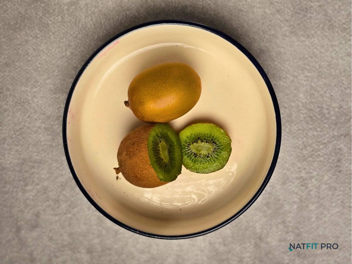 A whole kiwi and a sliced kiwi showing its vibrant green interior, placed on a cream platea nutrient-dense fruit and Vitamin C superstar for tissue repair.