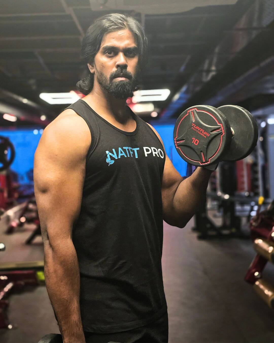 biceps-curl-dumbbell-gym-natfitpro Man performing dumbbell biceps curl in gym wearing Natfit Pro tank top