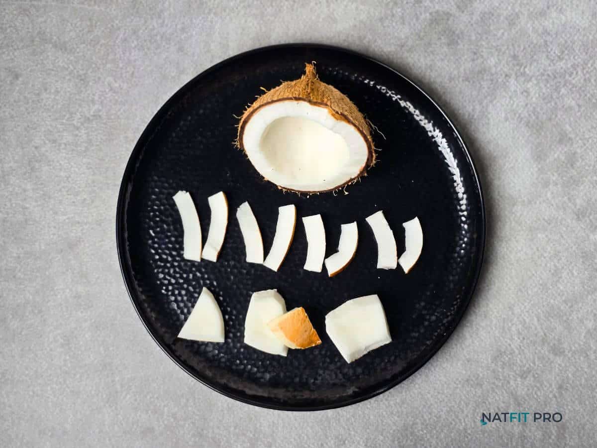 A black plate showing a cracked open fresh coconut with its white meat sliced, a high-calorie fruit perfect for a healthy weight gain diet.