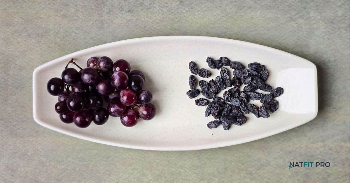 A direct comparison of fresh red grapes and dried black raisins on a white platter to show the difference in volume.