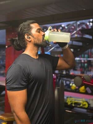A lifter drinking from a shaker bottle during his workout to stay hydrated.