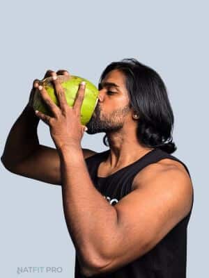 A lifter drinking directly from a fresh coconut for natural post-workout rehydration and electrolyte replenishment.