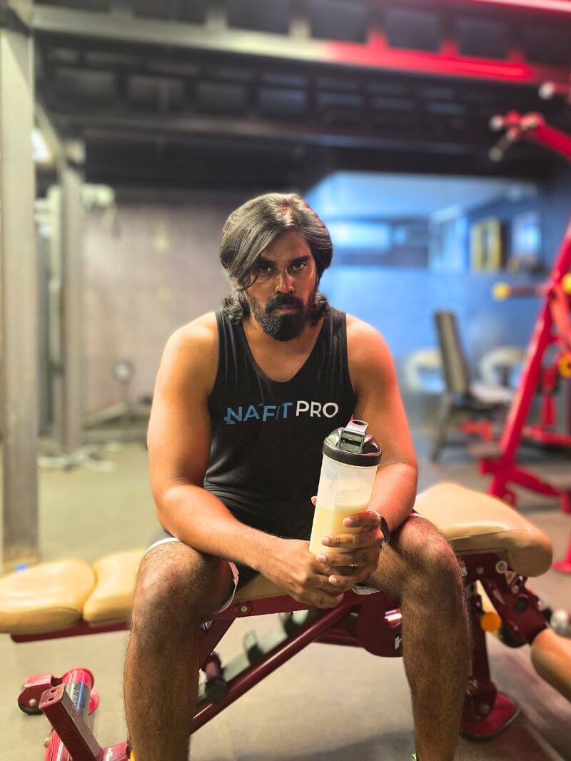 Tamil in NatFit Pro tank top sitting on bench holding a gym shaker bottle after workout