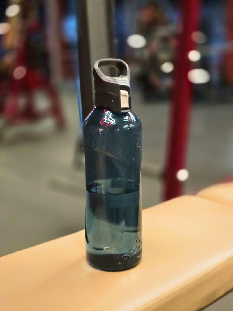 Reusable water bottle with secure flip-top lid placed on a gym bench