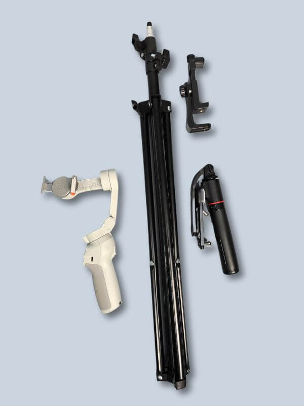 Flat lay image showing a full tripod kit, including a foldable tripod stand, smartphone holder, handheld tripod, and a white gimbal, arranged neatly on a soft blue background.